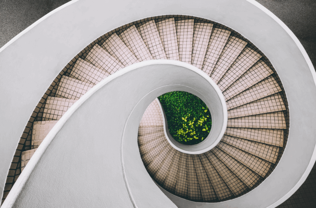 Zenith view of a white and brown concrete spiral stairs that lead to a patch of green.