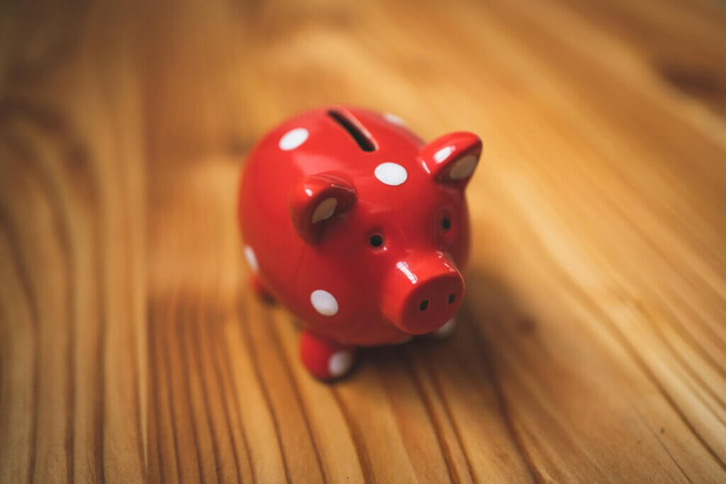 Red piggy bank with white spots on a wooden surface.