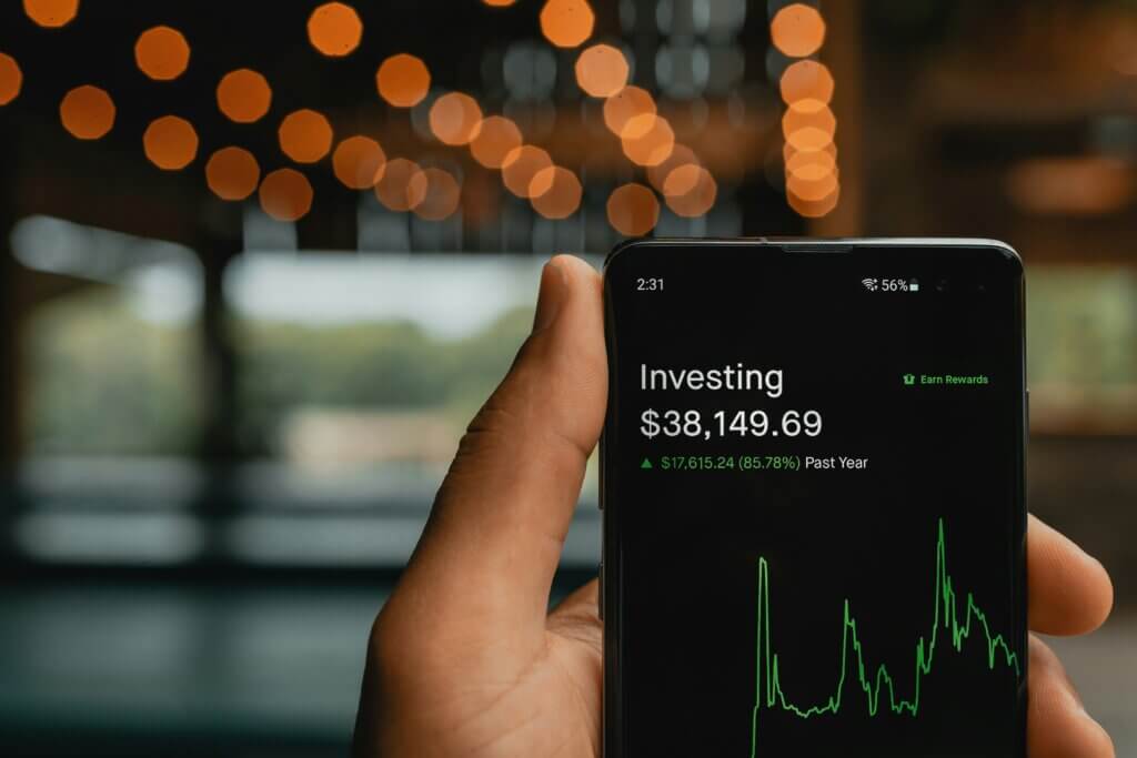 A hand holding a smartphone displaying an investing for beginners screen with a positive return.