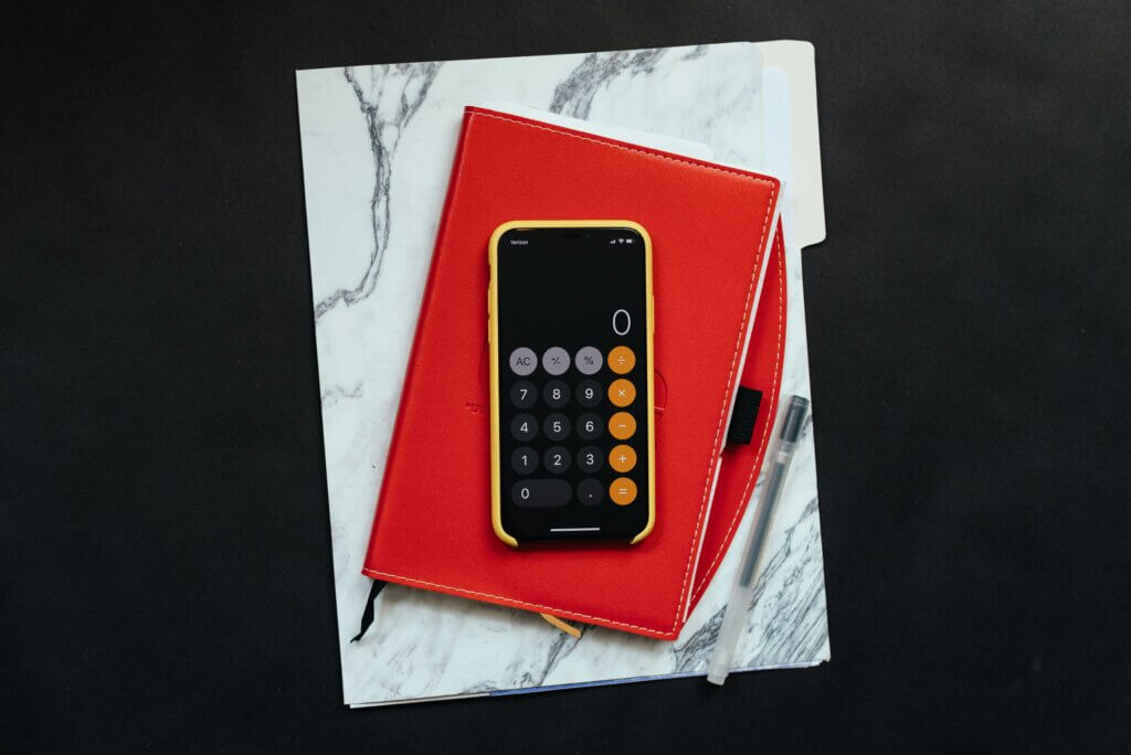 Smartphone open to calculator app showing a zero total, pen, and red folder on a black surface.