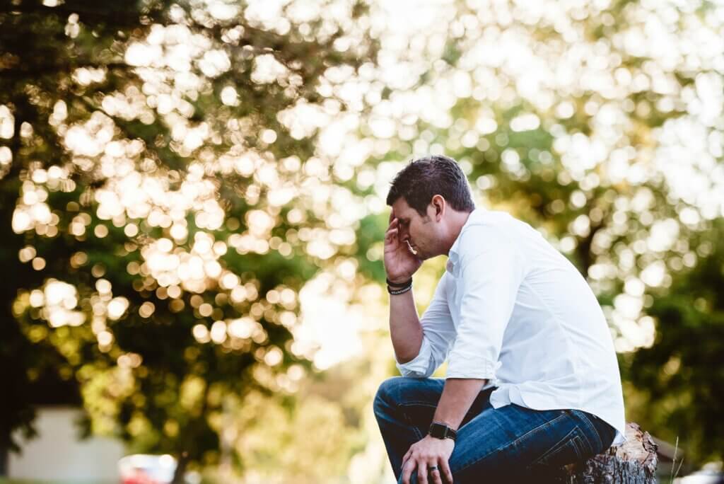A man is lost in thought in the woods.