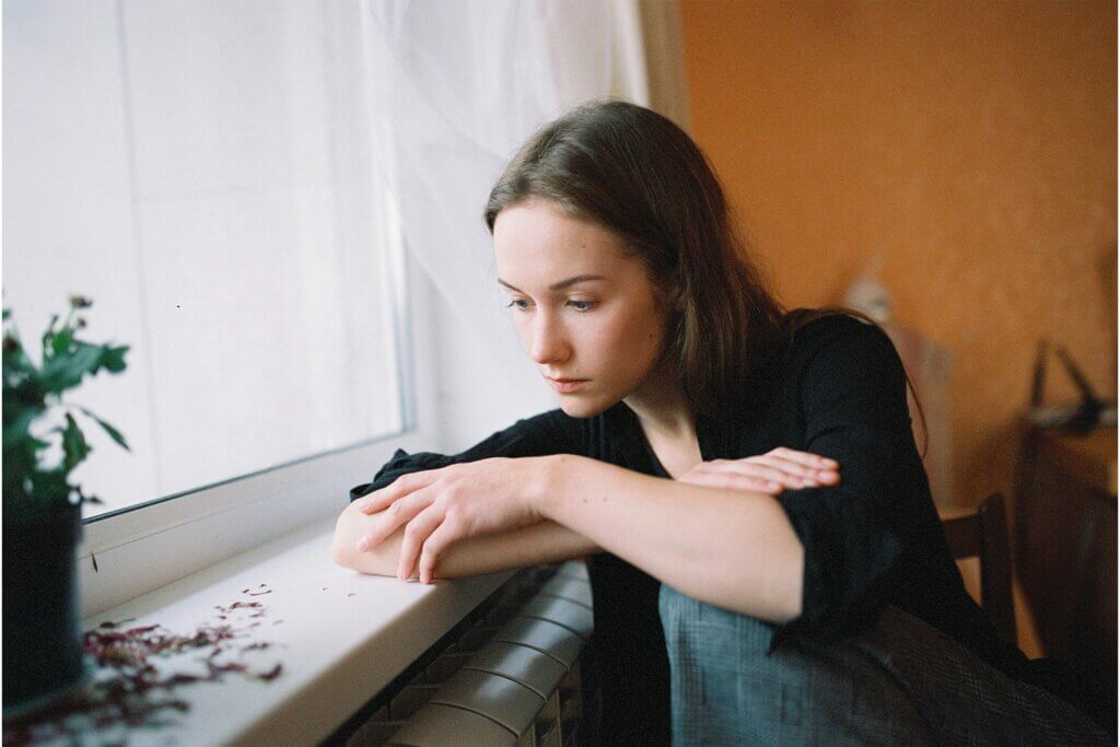 Woman sitting by a window sill gazing sadly out the window