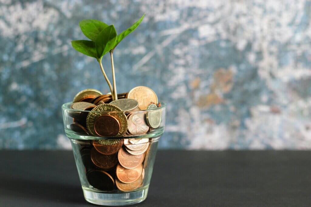 Green seedling in a glass filled with coins on a dark surface with abstract background.