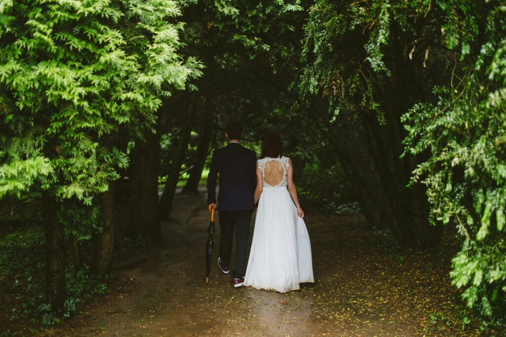 A man and a woman are just married and are walking into a forest together, back against the camera.