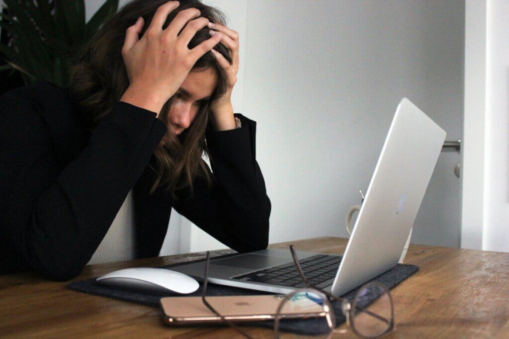 Stressed out woman with head in hands sitting in front of a laptop at a table.