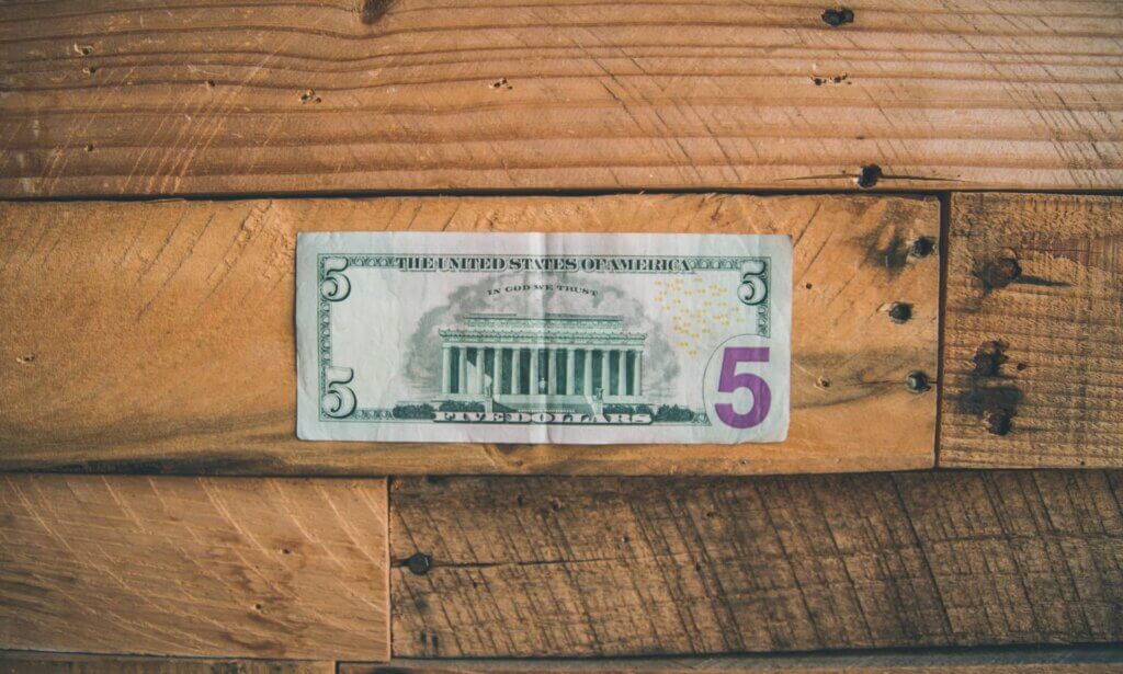 A five US dollar bill on a wooden surface.