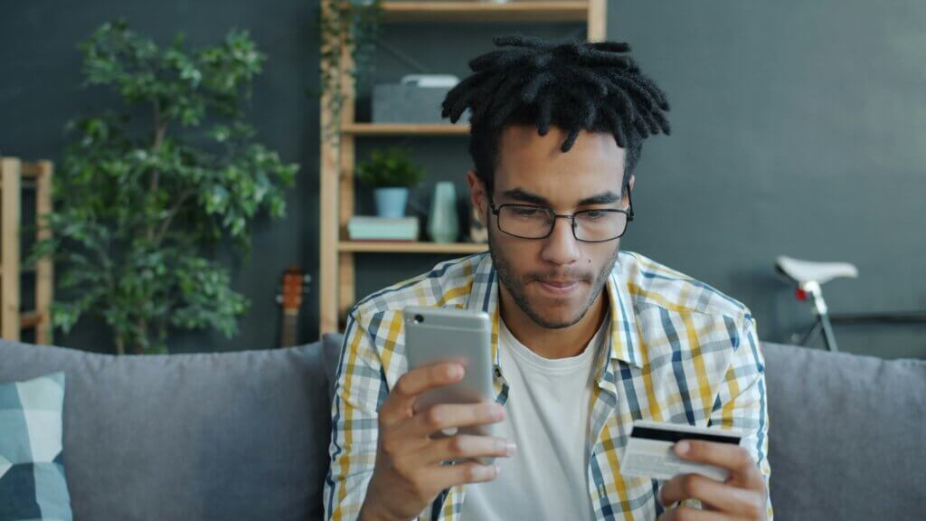 Person holding smartphone and credit card on couch